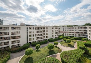 Ein mehrstöckiges Wohngebäude mit Balkonen, einem zentralen Innenhof mit Bäumen und blauem Himmel.