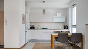 A modern kitchen with white cabinets, a wooden dining table with two chairs, and a pendant light. - Kolska Charming Apartment (Warszawa)