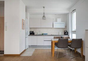 Eine moderne Küche mit weißen Schränken, einem Holzespeisetisch mit zwei Stühlen und einer Pendelleuchte.