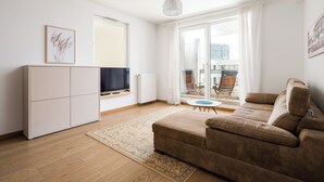 A modern living room with a sofa, a TV, a cabinet, and a view of the outdoors. - Kolska Charming Apartment (Warszawa)