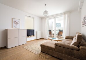 Ein modernes Wohnzimmer mit Sofa, Fernseher, Schrank und Blick ins Freie.