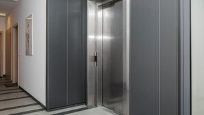 A modern elevator with metallic walls and a reflective surface, situated in a hallway with a patterned floor. - Kolska Charming Apartment (Warszawa)