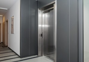 Ein moderner Aufzug mit metallischen Wänden und einer spiegelnden Oberfläche, gelegen in einer Diele mit einem gemusterten Boden.