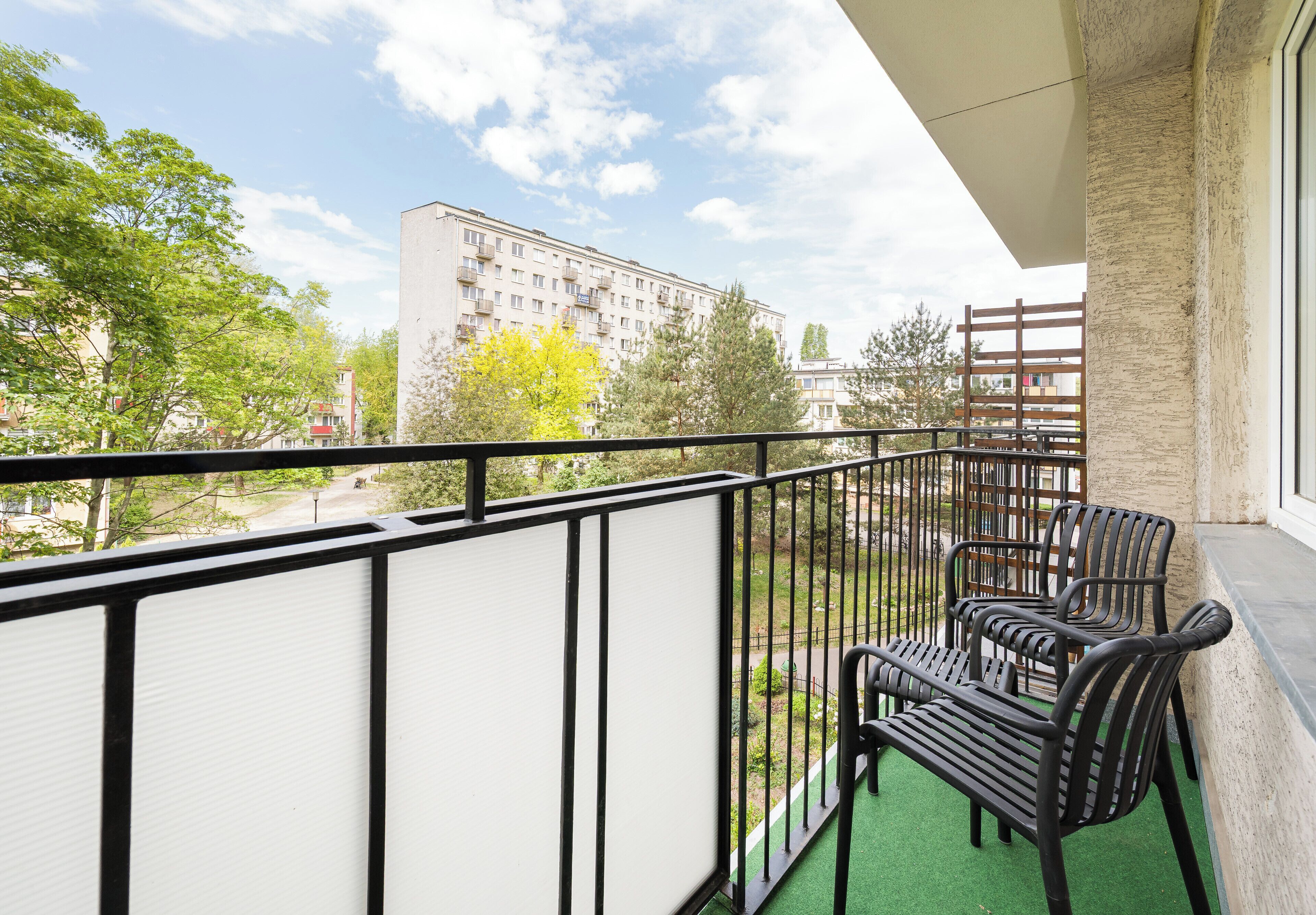 A balcony with a view of a building, a green artificial turf, and a wooden fence.