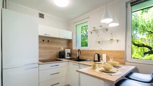 Una cucina compatta con mobili bianchi, un piano di lavoro in legno, una macchina per il caffè e una finestra vista verde.