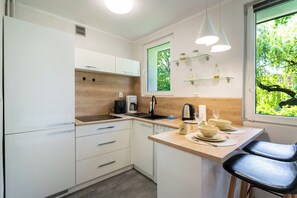 A compact kitchen with white cabinets, a wooden countertop, a coffee maker, and a window with a view of greenery. - Gorzołki Comfort Studio (Gliwice)