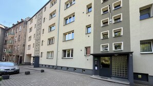 Un edificio residenziale a più piani con vialetto lastricato, un'auto parcheggiata a sinistra e un cancello.