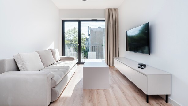Ein modernes Wohnzimmer mit einer Couch, einem Couchtisch, einem Fernseher und einem Balkon mit Blick.
