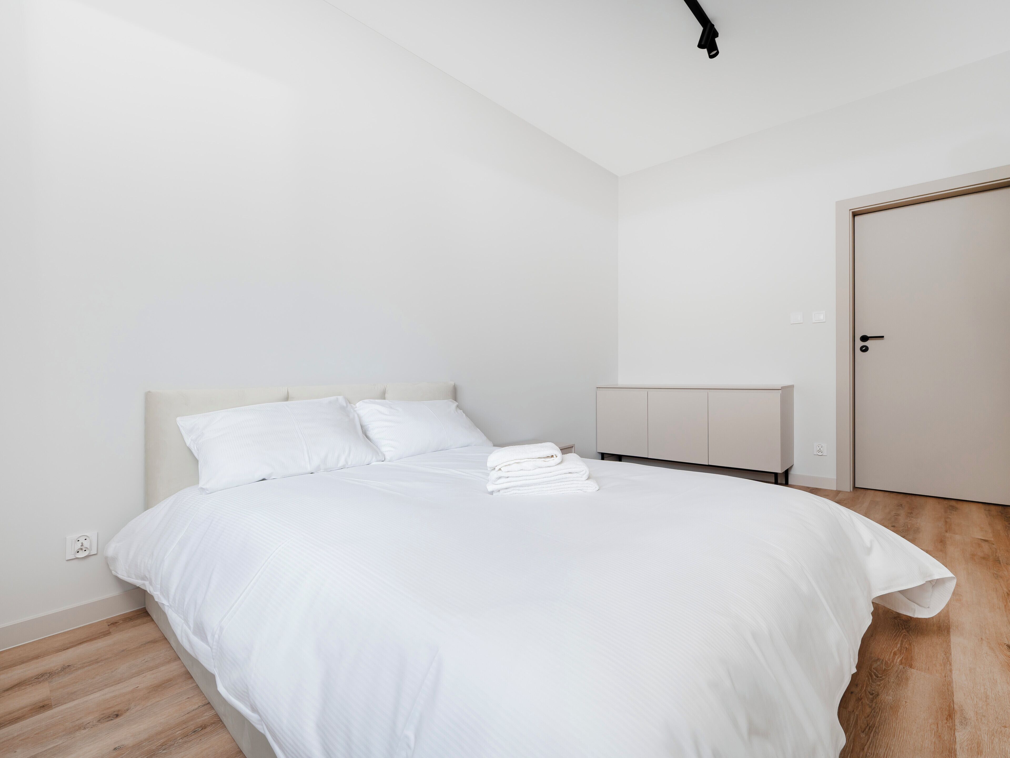 Een minimalistische slaapkamer met een bed, nachtkastje en een deur.