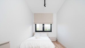 Ein Schlafzimmer mit Bett, Fenster, Deckenlampe und Holzboden.