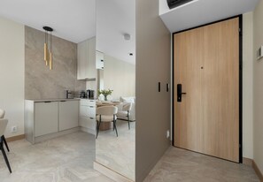 Eine moderne Küche mit Marmor-Spritzschutz, ein Essbereich mit weißem Tisch und Stühlen sowie eine Holztür.
