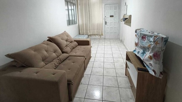 Una sala de estar con un sofá, una mesa con mantel estampado, una puerta y una ventana con cortinas.