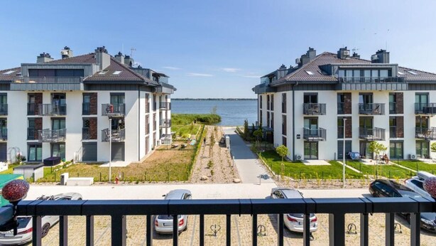 A modern apartment building with balconies, a parking area, and a view of the water. - Family Apartment for 4 by the Water (Dziwnów)