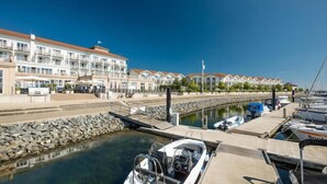 A marina with boats docked, a stone wall, and a row of white buildings with balconies. - Lindner Hotel Boltenhagen (Boltenhagen)