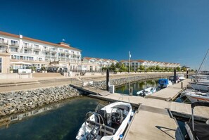 Un puerto deportivo con barcos amarrados, un muro de piedra y una hilera de edificios blancos con balcones.