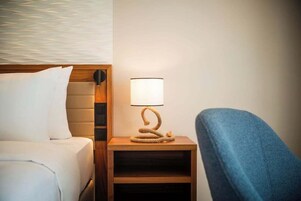 A hotel room with a bed, a nightstand with a lamp, and a chair.