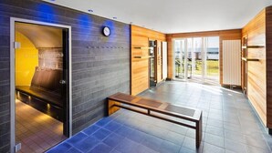 A modern hotel lobby with a bench, a clock, and a view of the outdoors. - Lindner Hotel Boltenhagen (Boltenhagen)