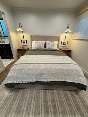 Ein ordentlich eingerichtetes Schlafzimmer mit einem Bett, zwei Nachttischen, einem Schminktisch und einem gerahmten Bild an der Wand.