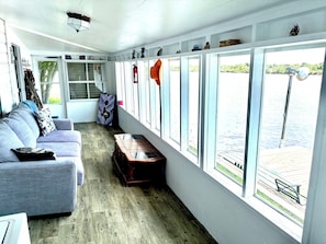 Una habitación con un sofá gris, un cofre de madera y un ventanal con vistas a un muelle y al agua.