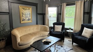 Un salon avec un canapé beige, un fauteuil noir, une table basse noire et un lustre.