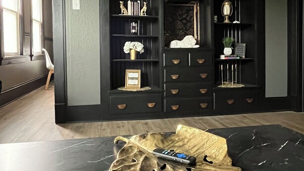 Une pièce avec une table en marbre noir, une cheminée avec un manteau de cheminée et une bibliothèque agrémentée d’objets décoratifs.
