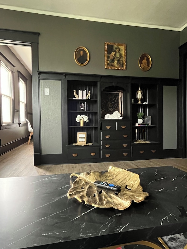Una habitación con una mesa de mármol negro, una chimenea con repisa y una estantería decorada con objetos.