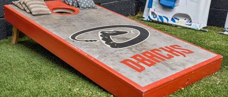 A concrete shuffleboard table with a logo and text, surrounded by grass and a black wall.