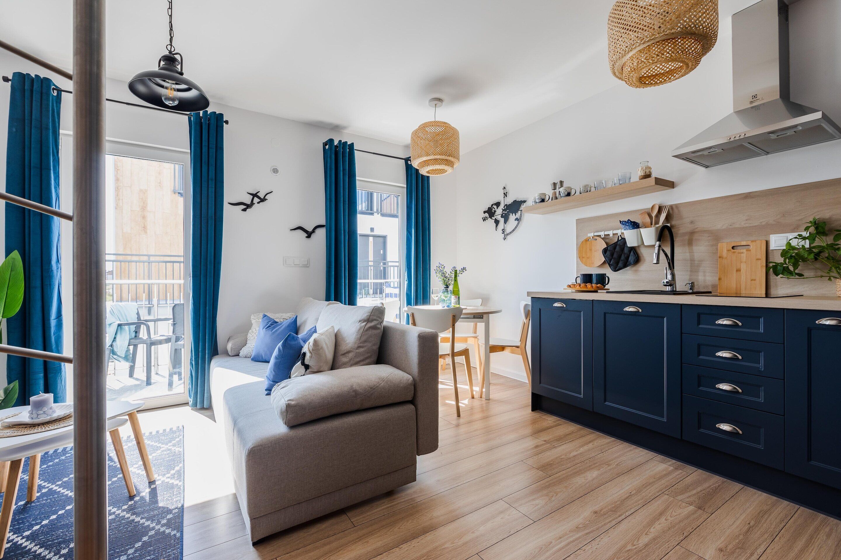 A modern living room with a sofa, dining table, and kitchen area with cabinets and a hanging light fixture.