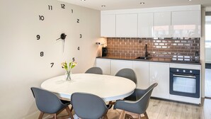Een moderne keuken met witte kastjes, een tegelwand van baksteen en een ronde eettafel met stoelen.