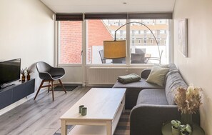 A modern living room with a sofa, a coffee table, a TV, and a large window with a view of buildings. - Awesome apartment in Faaborg with sauna (Faaborg)