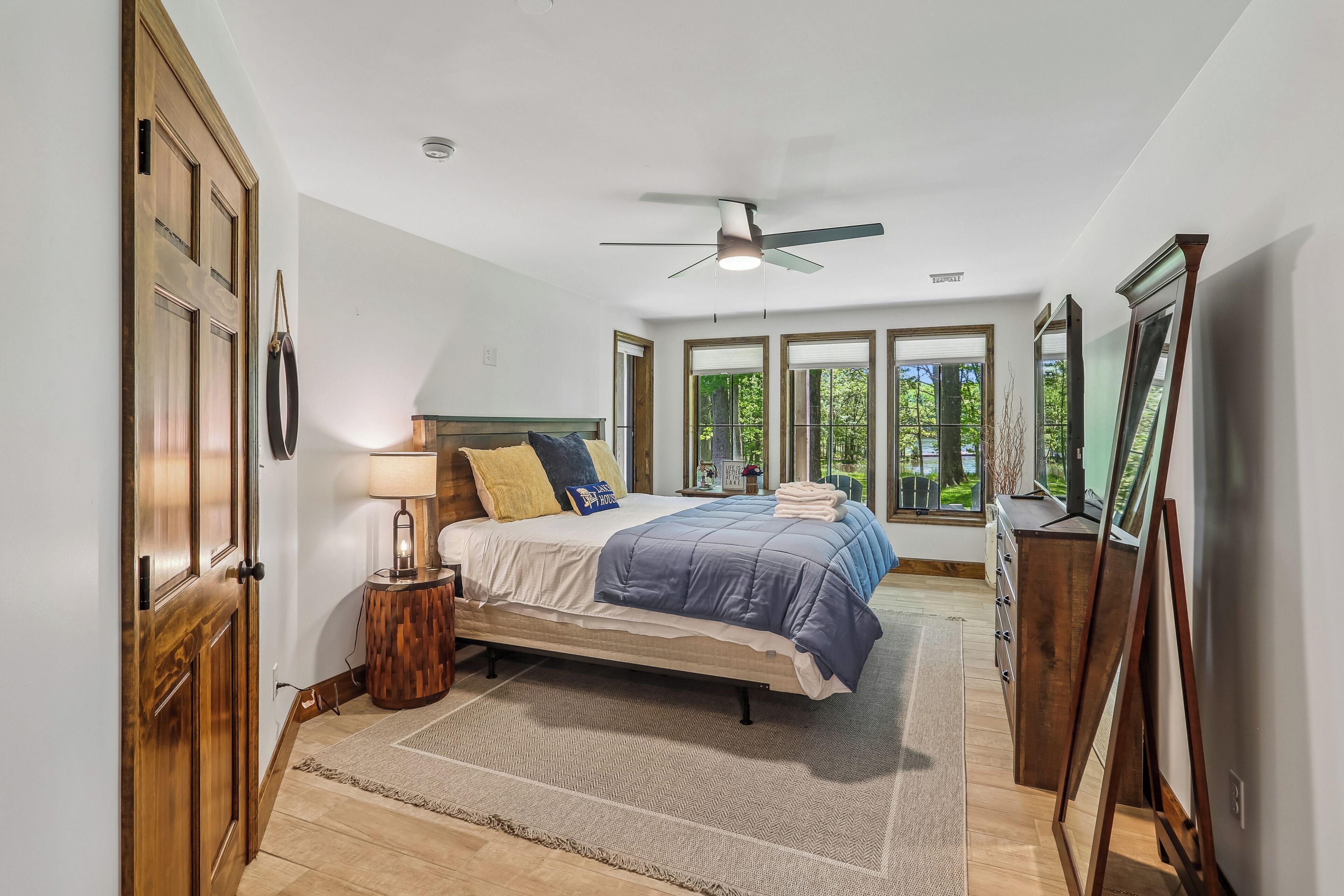 A bedroom with a bed, a ceiling fan, a wooden door, and large windows.