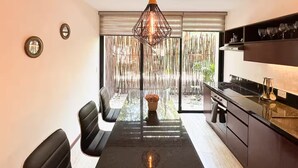 A modern kitchen with a dining area, a hanging light fixture, and a view through a bamboo screen. - Beautiful home in the jungle (Tulum)