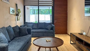 A modern living room with a grey sofa, a wooden coffee table, and a wooden side table with a small screen. - Beautiful home in the jungle (Tulum)