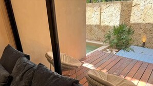 A modern outdoor seating area with a wooden deck, a pool, and a stone wall. - Beautiful home in the jungle (Tulum)