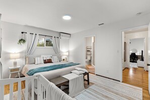 A modern bedroom with a large bed, bedside tables, a nightstand, a window with curtains, a ceiling light, and a view of a bathroom and hallway. - Spacious 4BR/2BTH King Bed Ranch Style, Prime Area (La Mesa)
