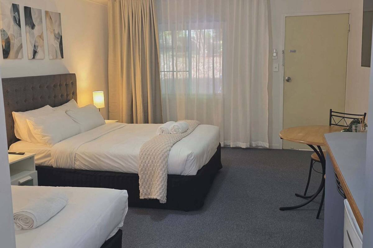 A hotel room with two beds, a desk, a chair, and a door.