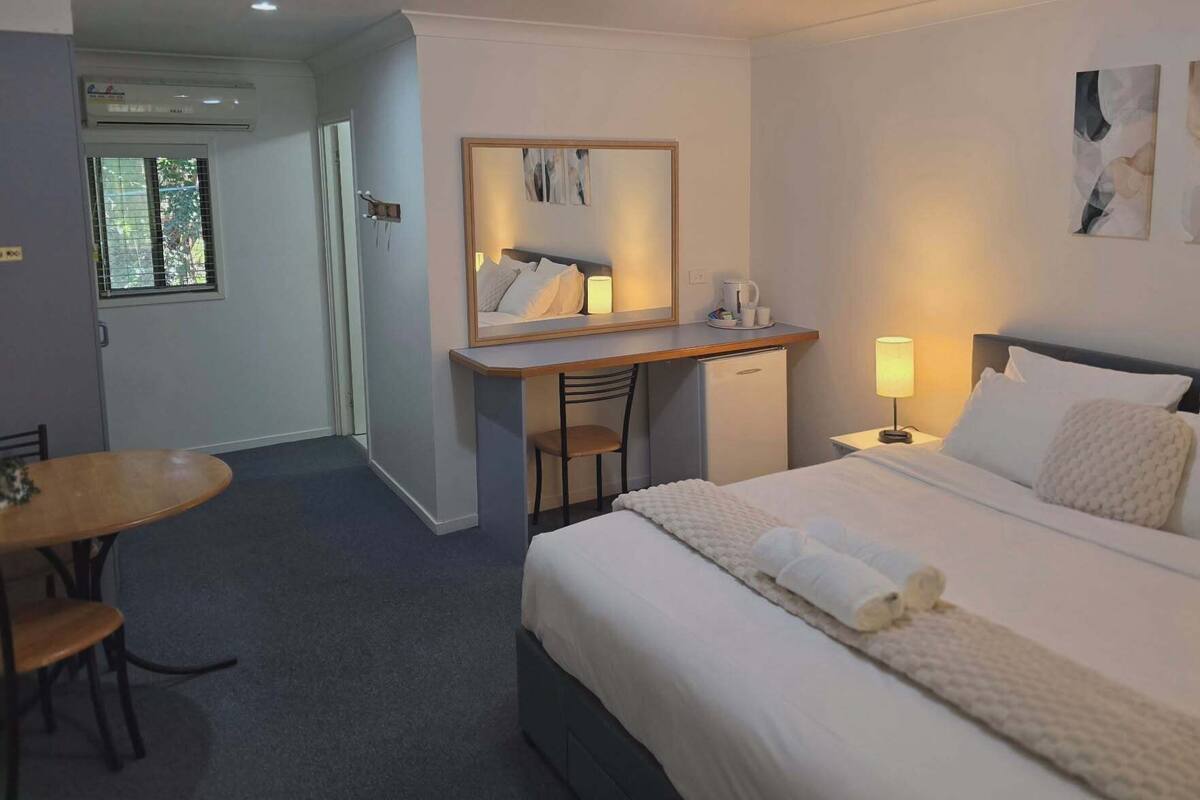 A hotel room with a bed, a desk with a chair, a small refrigerator, a coffee maker, and a mirror.