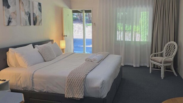 Una habitación de hotel con cama, una silla, un escritorio y una ventana con cortinas.