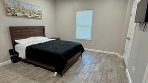 Ein Schlafzimmer mit einem Bett, einem Deckenventilator, einem Fenster mit Jalousien und einer Tür, über der sich ein Fernseher befindet.