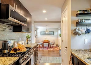 A modern kitchen with dark cabinets, a granite countertop, and a dining area with a table and chairs. - Cape Cod ať South River USNA Commissioning Week! (Riva)