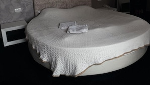 A bedroom with a large bed, a headboard, a bedside table, a mirror, and a wall-mounted light fixture. - Agusta Spa Hotel (Veliko Tarnovo)