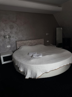 A bedroom with a large bed, a headboard, a bedside table, a mirror, and a wall-mounted light fixture. - Agusta Spa Hotel (Veliko Tarnovo)