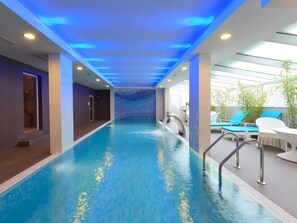 A swimming pool with a blue interior, surrounded by a lounge area with white furniture and a glass ceiling. - Agusta Spa Hotel (Veliko Tarnovo)