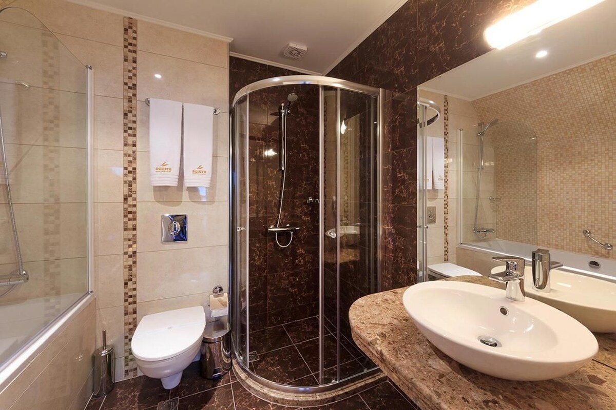 A modern bathroom with a glass-enclosed shower, a white toilet, and two sinks.