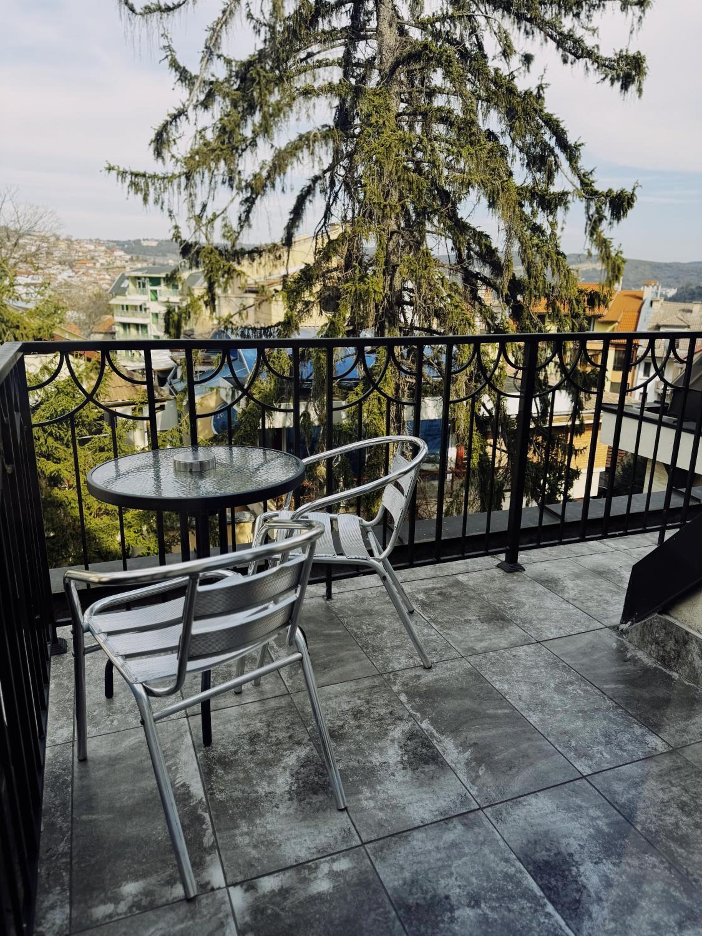 Un balcón con una mesa redonda y dos sillas, con vistas a una zona residencial con casas y árboles.