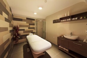 A modern bathroom with a glass-enclosed shower, a white massage table, and a vanity with a sink and toiletries. - Agusta Spa Hotel (Veliko Tarnovo)