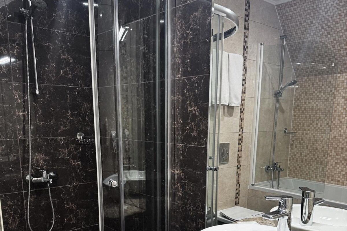 A modern bathroom with a glass-enclosed shower, a granite countertop, and a large mirror.