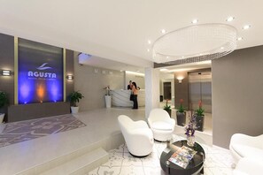 A hotel reception area with a reception desk, white chairs, a coffee table, and a reception sign. - Agusta Spa Hotel (Veliko Tarnovo)