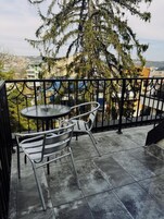 A balcony with a round table and two chairs, overlooking a residential area with houses and trees.
