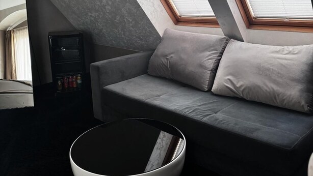 A modern loft bedroom with a sloped ceiling, a grey sofa, a round coffee table, and skylights. - Agusta Spa Hotel (Veliko Tarnovo)